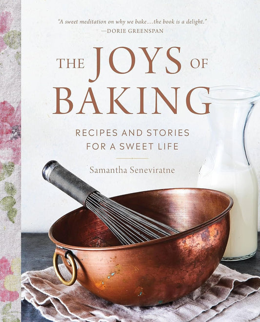 Cover of "The Joys of Baking: Recipes and Stories for a Sweet Life" by Samantha Seneviratne, featuring a copper mixing bowl with a whisk inside and a glass of milk next to it on a linen cloth.
