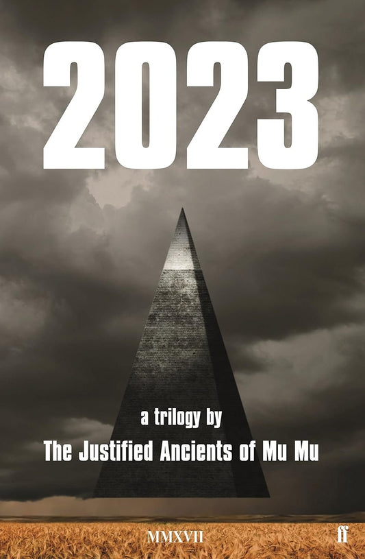 Book cover of "2023: A Trilogy" by The Justified Ancients of Mu Mu featuring a towering black pyramid against a stormy sky over a golden wheat field.