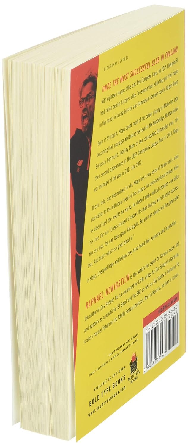 A book stands angled showing its spine and pages. The spine is red with a portrait of Jürgen Klopp, the bearded Liverpool manager in glasses and a black suit. "Bring the Noise: The Jürgen Klopp Story" by Raphael Honigstein, title and text.